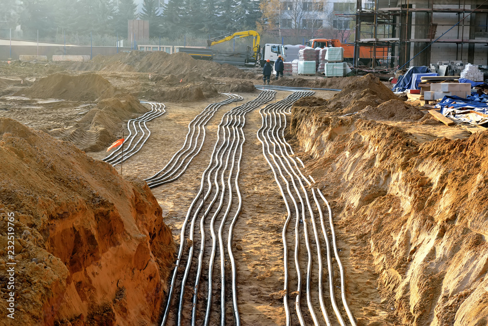 Several rows of electrical conduits are laid in trenches at a construction site, showcasing commercial electrical services Arizona relies on, with workers and equipment visible in the background.