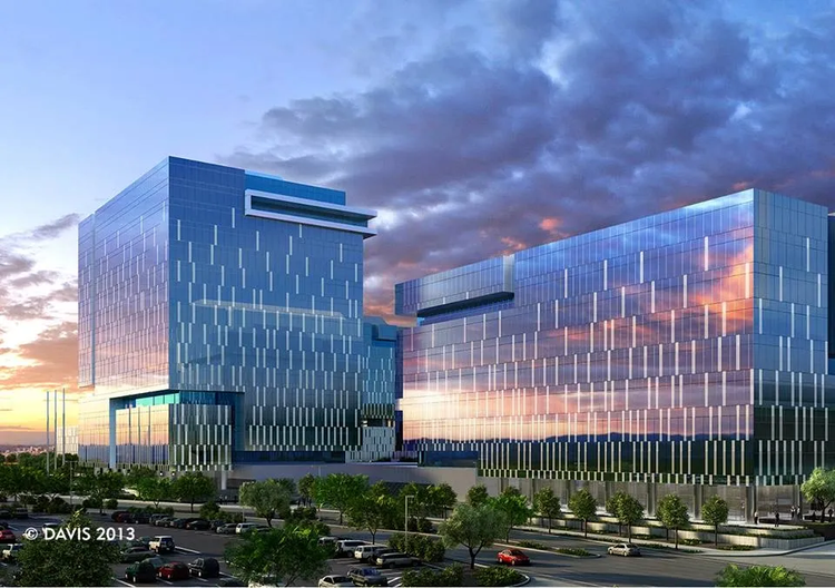 Two modern glass office buildings reflect a colorful sunset sky, with a busy parking lot and trees in the foreground—an impressive site often seen during major commercial electrical projects in Arizona.