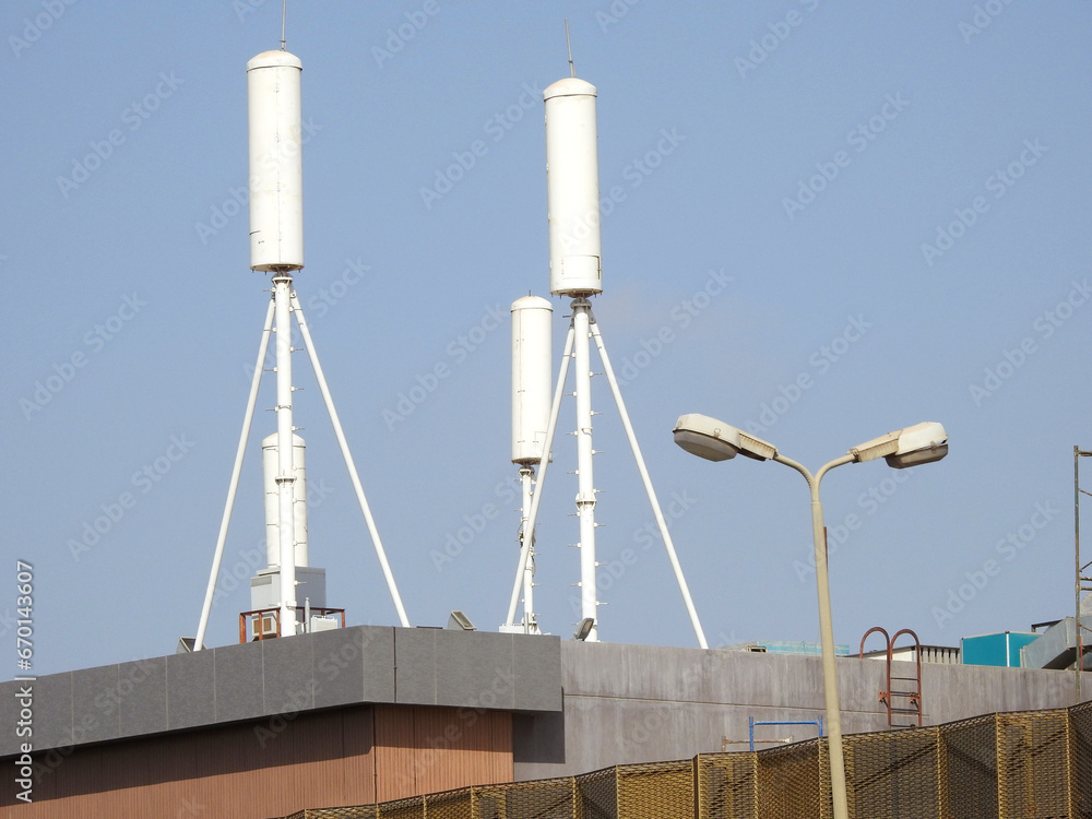 Two white cylindrical water tanks on tall metal supports are installed on the roof of a building, part of commercial electrical projects Arizona, with a street lamp in the foreground under a clear blue sky.