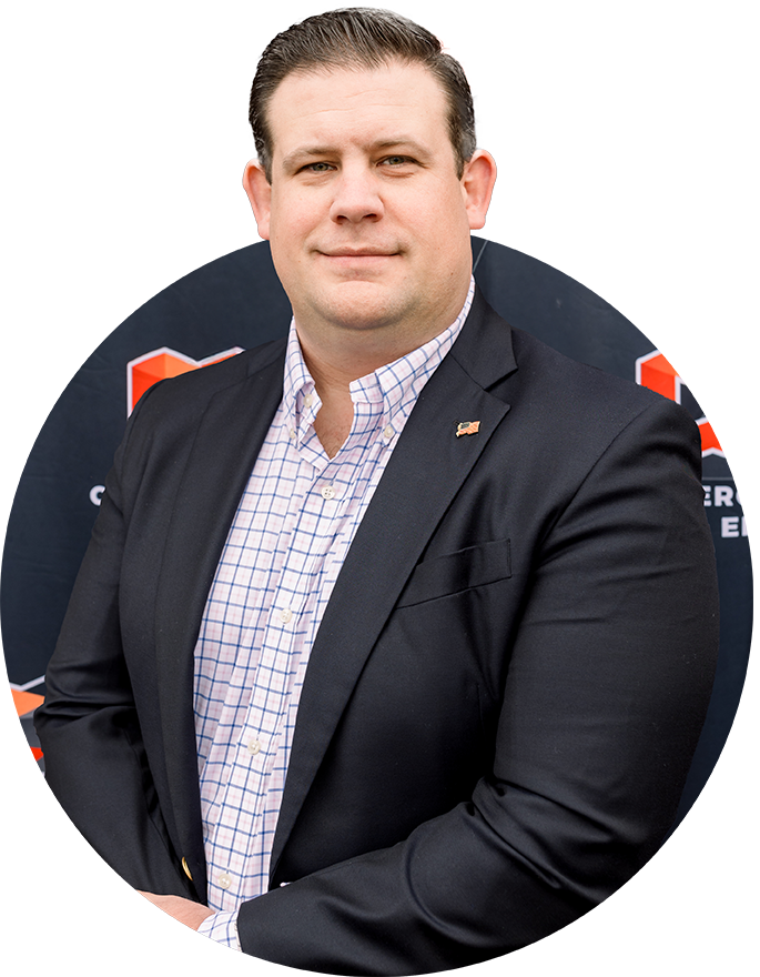A man in a suit stands with his hands folded in front of a branded Commercial Comm and Electric backdrop featuring orange and white geometric logos.